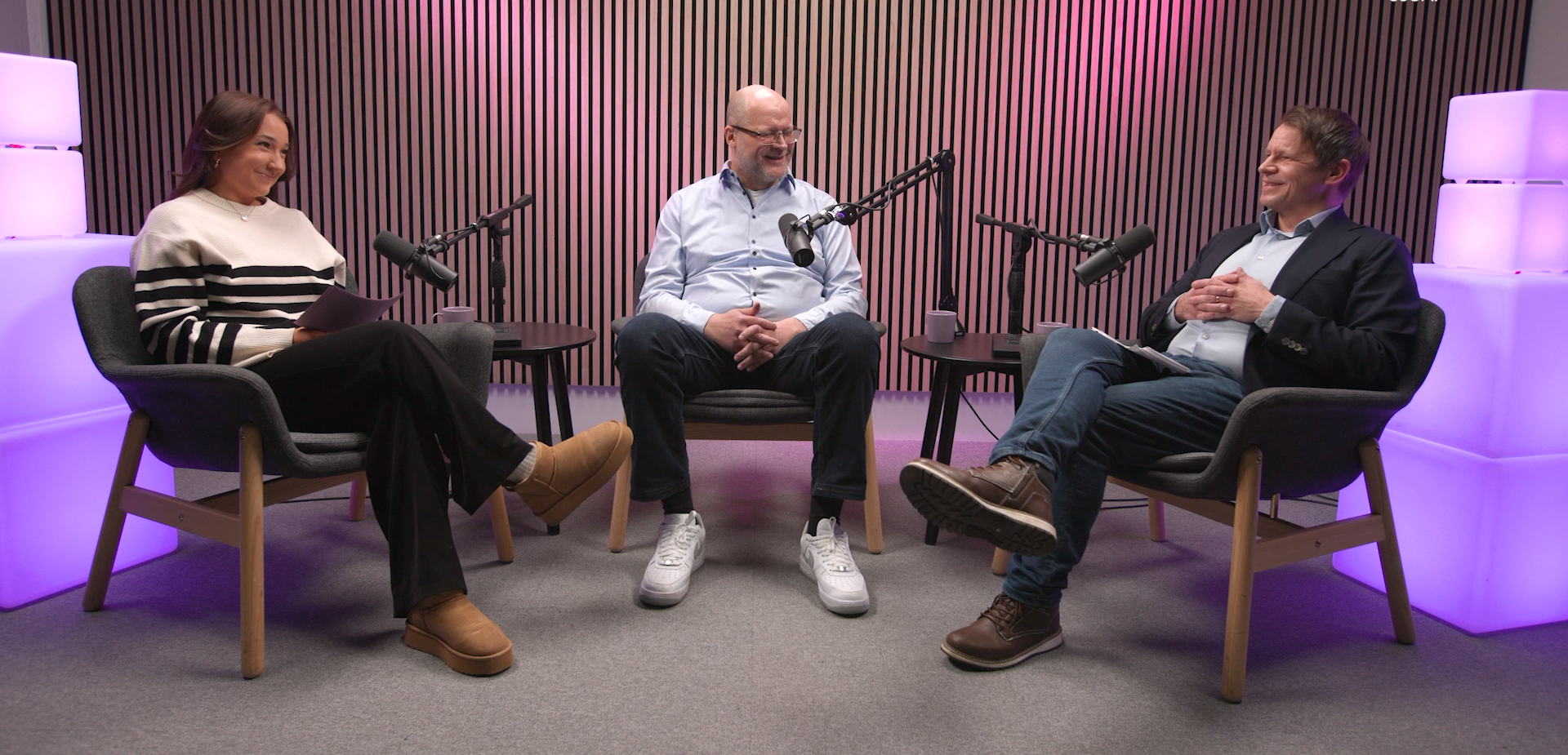 Three people sitting in a podcast studio smiling at each other.