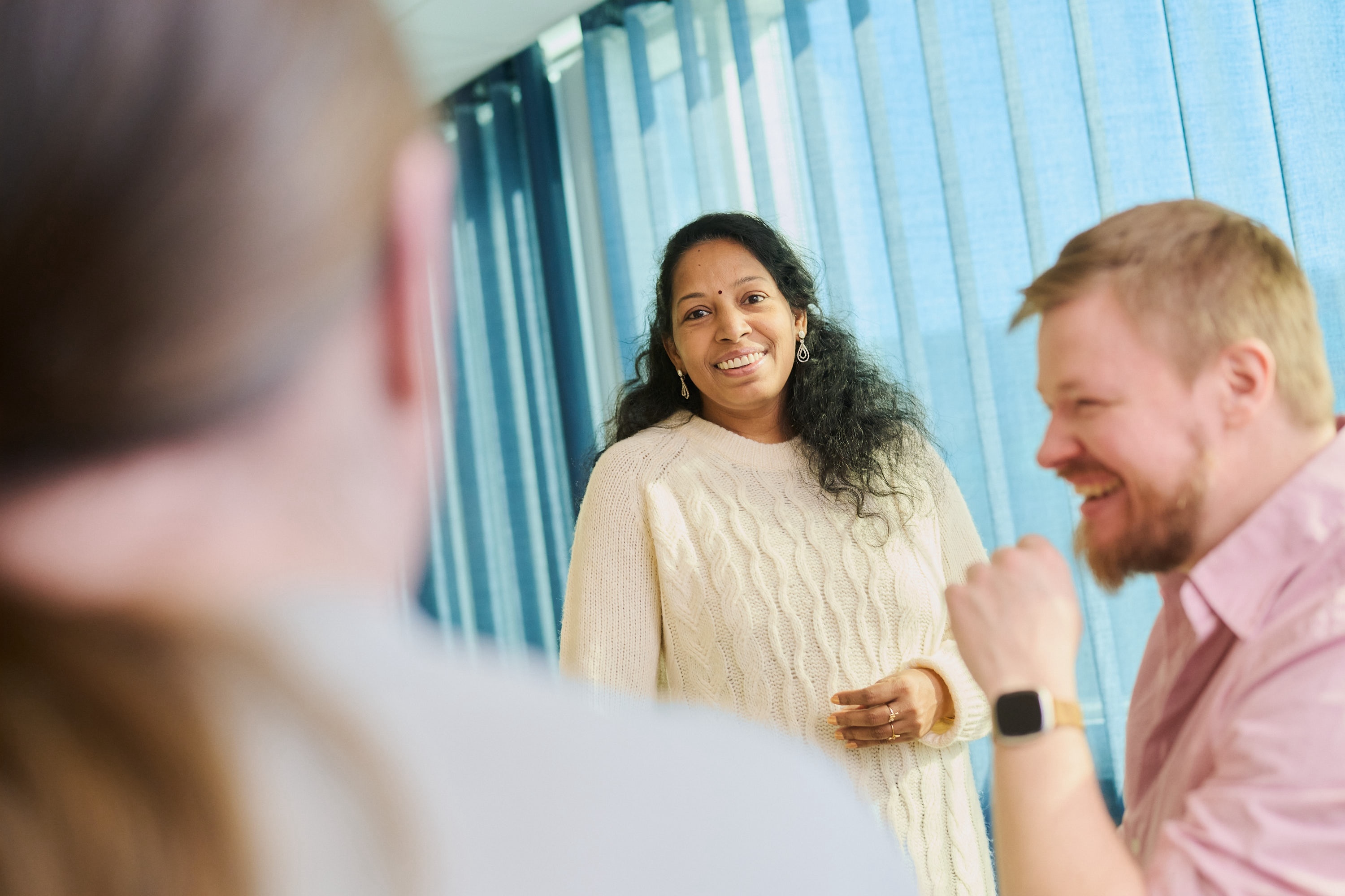 Three people in a meeting discussing and smiling at each other.